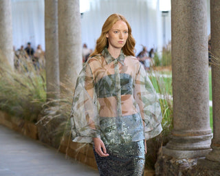 Woman in a stylish outfit standing in an outdoor setting with columns and greenery.